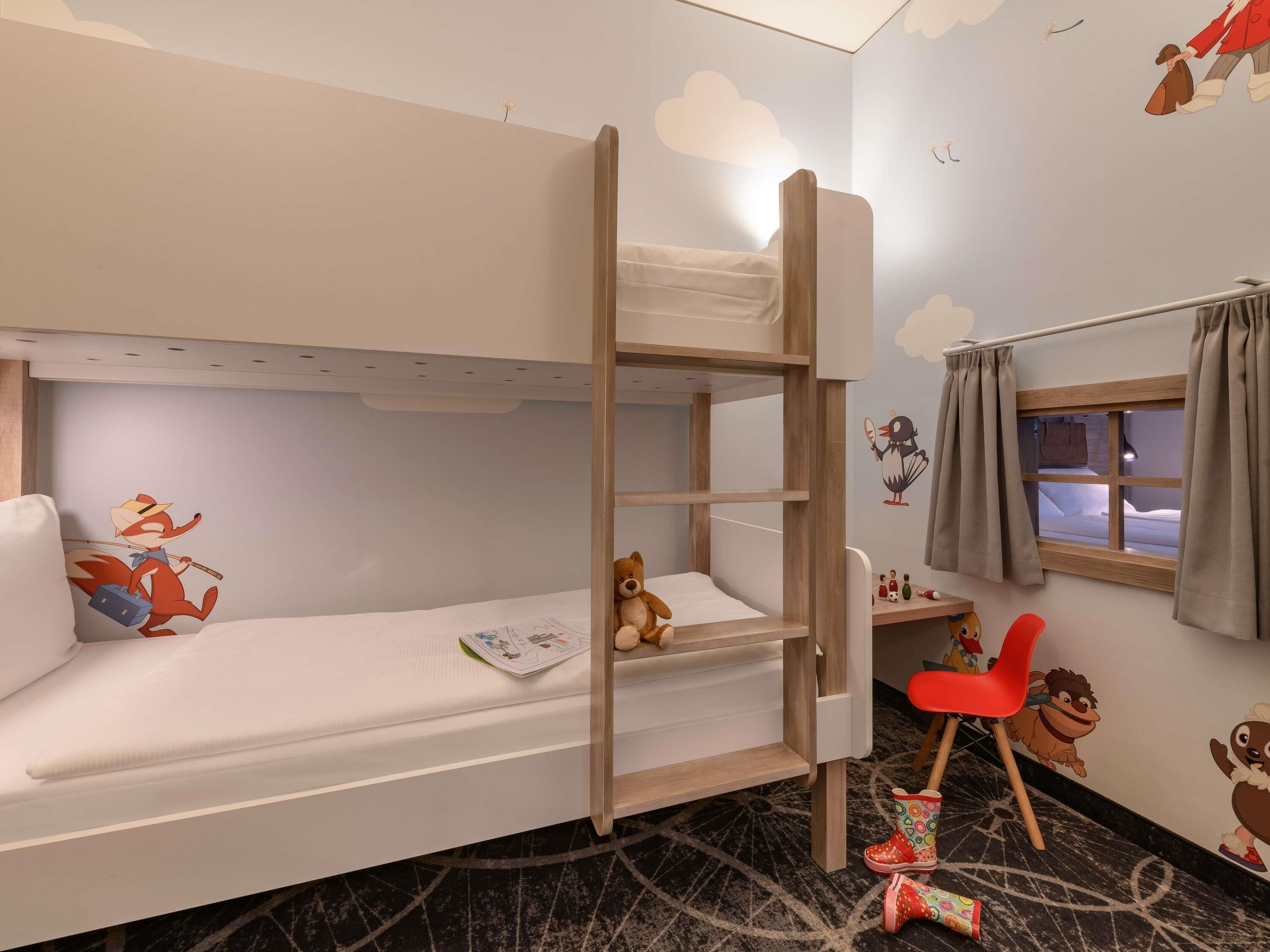 Une chambre avec un lit superposé, une fenêtre, une chaise rouge et des décorations murales à motifs de dessins animés.