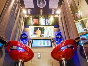 Een karaokezaal met een scherm waarop een optreden te zien is, twee rode stoelen en een bedieningspaneel.