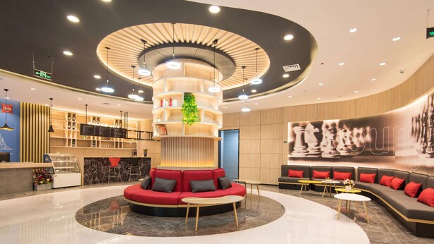 Un hall d’hôtel moderne doté d’un espace salon central, d’un comptoir d’accueil et d’une grande fresque murale.