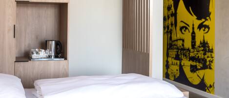 Una habitación de hotel con una cama, una cafetera en un estante y una pared decorada con un gráfico.