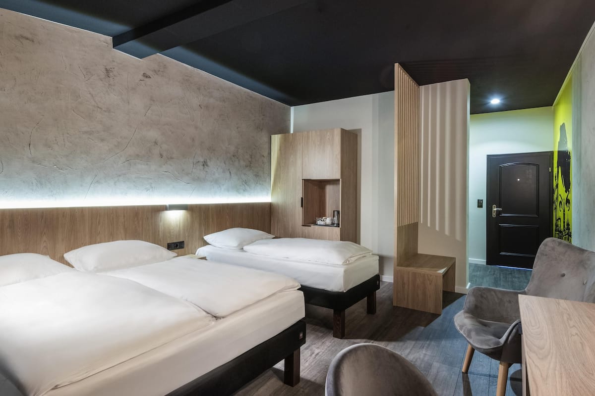 A modern hotel room with two beds, a wooden wardrobe, a desk, and a chair.