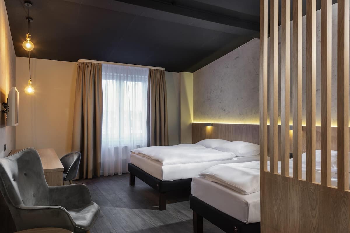 A hotel room with two beds, a desk, a chair, and a large window with curtains.