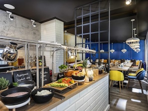 Un banco buffet con diversi cibi, una macchina per caffè e una zona con tavoli e sedie.