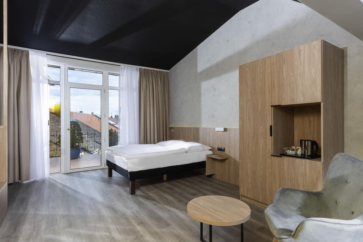 A modern bedroom with a bed, a round wooden table, a grey armchair, and a built-in wooden wardrobe.