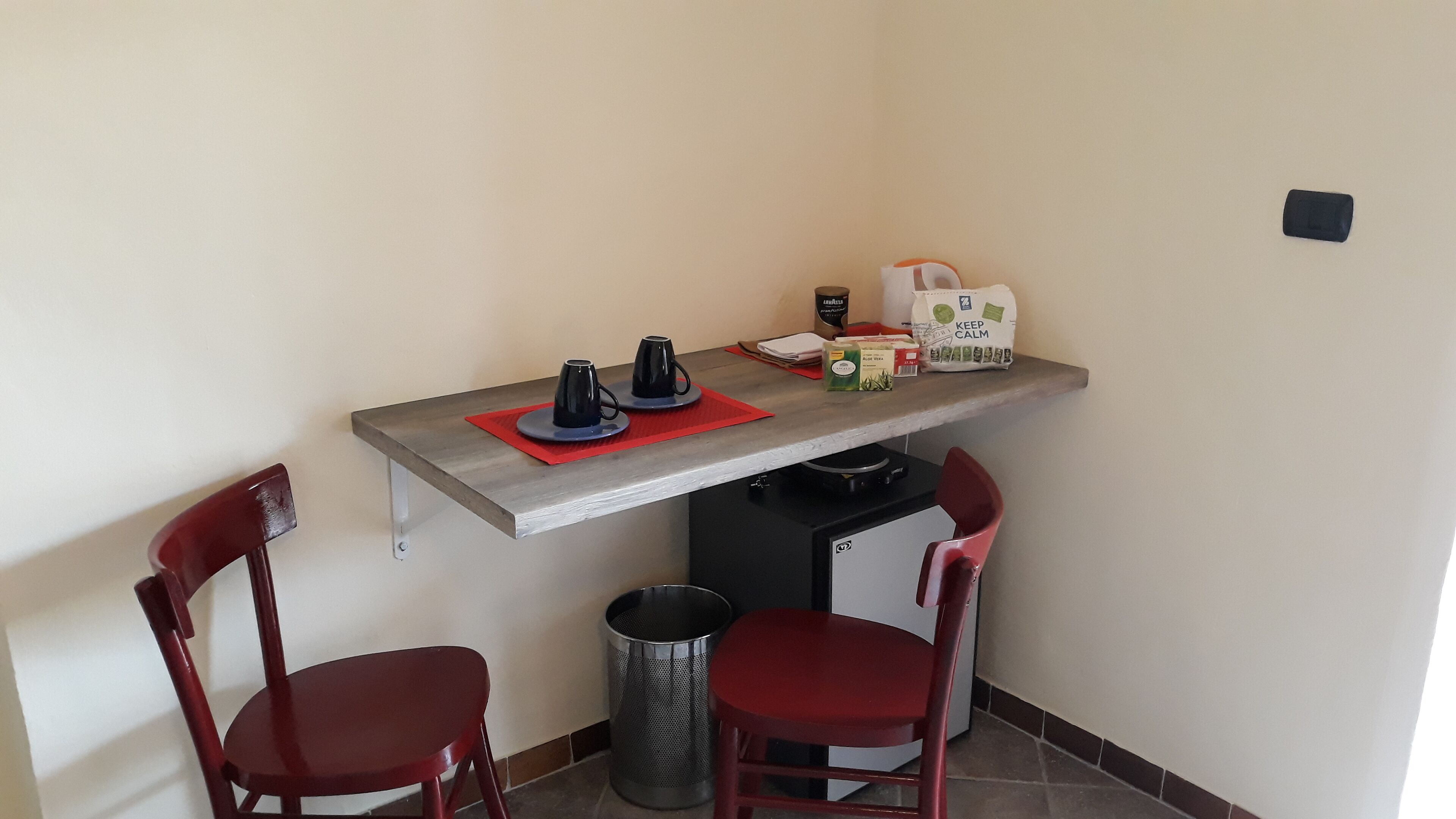 A small kitchenette area with a countertop, two red chairs, a trash can, and a coffee maker.