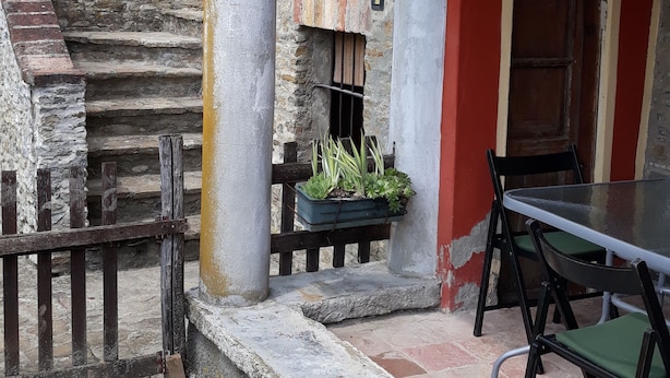 A stone staircase leading to a red-roofed building with a wooden fence, a table with chairs, and a hanging lantern. - Cascina Binelli (Dogliani)