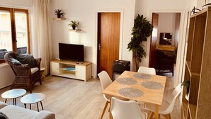 Una sala de estar con televisor, sofá y mesa de comedor con sillas.