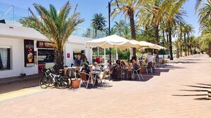Un café al aire libre con mesas y sillas, rodeado de palmeras y un cielo despejado.