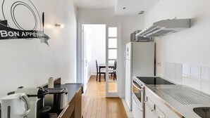 Eine moderne Küche mit Holzboden, einer Essecke mit Tisch und Stühlen und Blick durch eine offene Tür in einen hellen Raum.