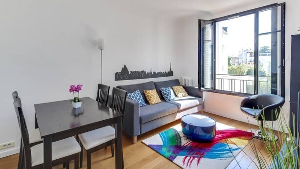 Ein modernes Wohnzimmer mit einer Couch, einem Esstisch und Stühlen. Ein großes Fenster bietet Blick auf die Stadt.