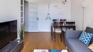 Ein Wohnzimmer mit Sofa, Fernseher, Esstisch mit Stühlen und einer Wand mit Dekoration.