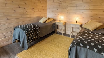 Ein Zimmer mit zwei Betten, jeweils mit einer Decke mit Sternenmuster, Holzwänden und zwei Nachttischen mit Lampen.