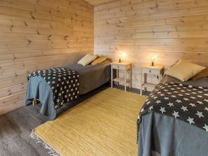 Une chambre avec deux lits, chacun recouvert d’une couverture ornée de motifs en forme d’étoiles, des murs en bois et deux tables de chevet avec des lampes.