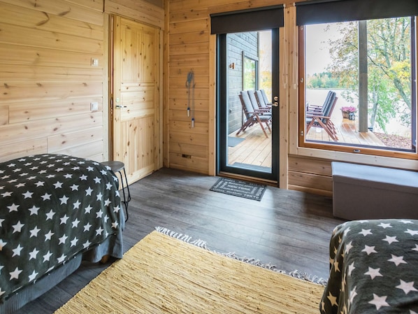 Une chambre avec deux lits, un plancher en bois, une porte donnant sur l’extérieur et une vue sur l’espace aménagé à l’extérieur.