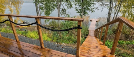 Une terrasse en bois qui mène à un quai surplombant un lac paisible, le tout entouré d’arbres.
