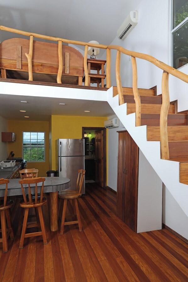 A kitchen with a wooden staircase, a dining area with stools, and a stainless steel refrigerator.