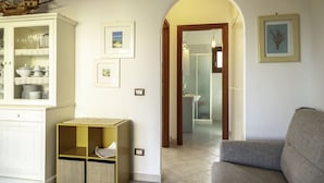 A living room with a sofa, a cabinet with dishes, and framed pictures on the wall. - Aria Di Vacanza - Mirtillo COD 9 (Olbia)