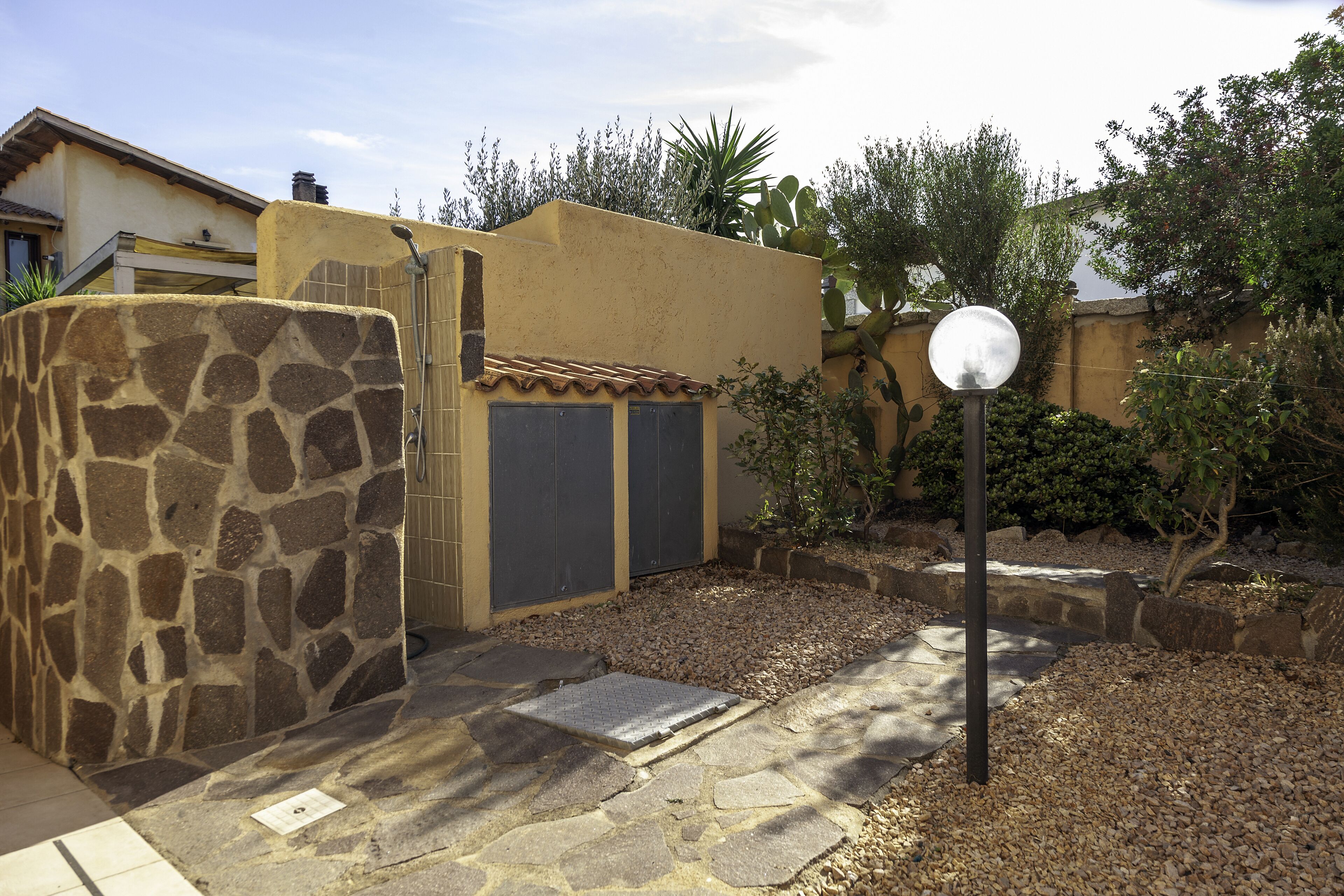 Un patio con un muro de piedra, una puerta metálica y un farol esférico.