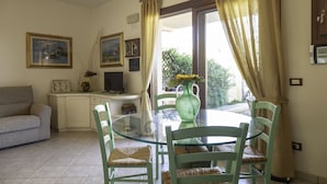 A dining area with a glass table, green chairs, and a vase with flowers. There is a sofa and a TV in the background. - Aria Di Vacanza - Mirtillo COD 9 (Olbia)