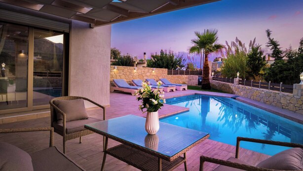 A poolside area with wicker furniture and a glass table, surrounded by stone walls and greenery. - Villa Elenitsa (Kissamos)