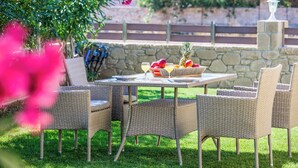 A wicker outdoor dining set with a stone wall and greenery in the background. - Villa Elenitsa (Kissamos)
