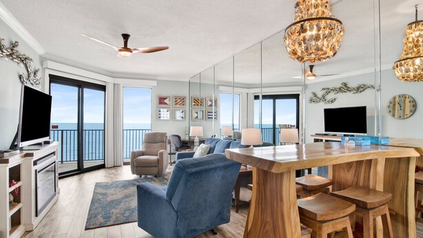 Uma sala de estar ampla com uma grande mesa de madeira, poltronas azuis e uma televisão.