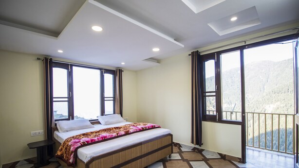 A bedroom with a bed, a small table, and a window with a view of a forested area. - Comfort Homestay (Dalhousie)
