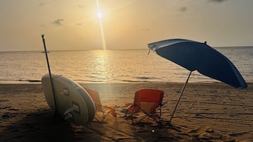 Uma praia com uma prancha de surf, um guarda-sol azul e uma cadeira vermelha.