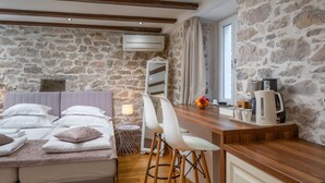 Une pièce chaleureuse avec un mur en pierre, un lit recouvert de linge blanc, un comptoir de bar en bois et une petite table avec une lampe.