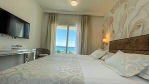 Une chambre d’hôtel avec un lit, un bureau, une télévision et une vue sur la mer.