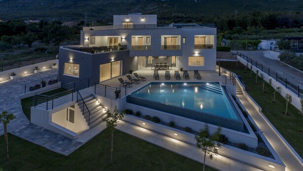 Une maison moderne à deux étages, dotée d’une piscine, d’un espace extérieur aménagé et d’un patio bien éclairé.