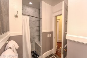 A bathroom with a shower, a towel rack, and a door leading to another room.
