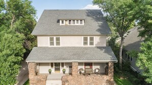 A two-story house with a stone foundation, a front porch with seating, and a small attached garage.