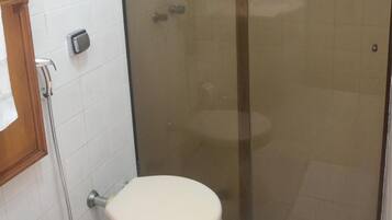 A bathroom with a toilet, a glass-enclosed shower, and a white tiled wall.