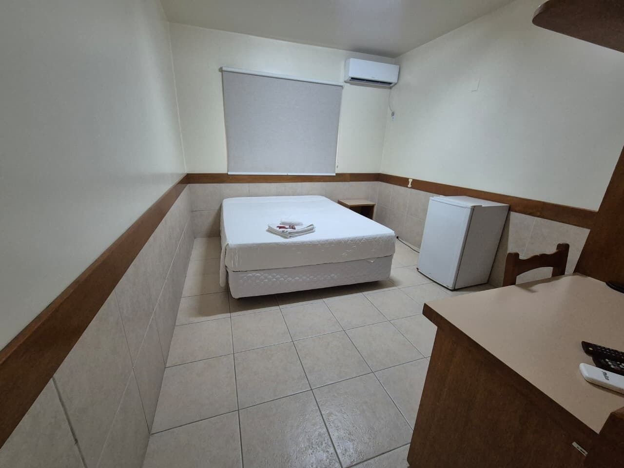 Una habitación pequeña con cama, una mesita, una silla y un refrigerador.