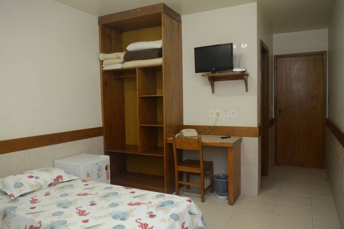 Un dormitorio con cama, escritorio, televisor, armario y puerta.