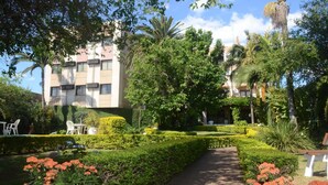 Un jardín bien cuidado con un camino, setos perfectamente recortados y un edificio de varios pisos con unidades de aire acondicionado.