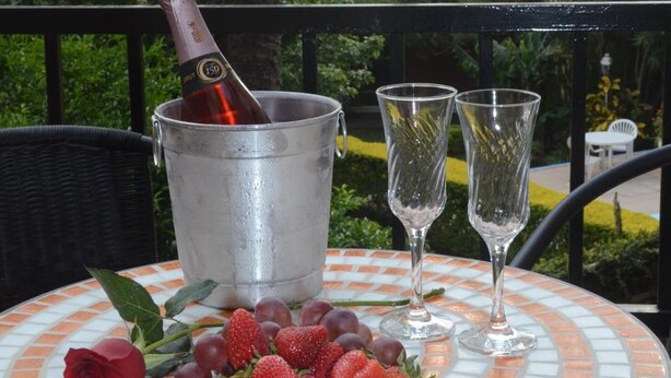 Una mesa con una botella de champán, dos copas, un plato de fresas y una rosa.