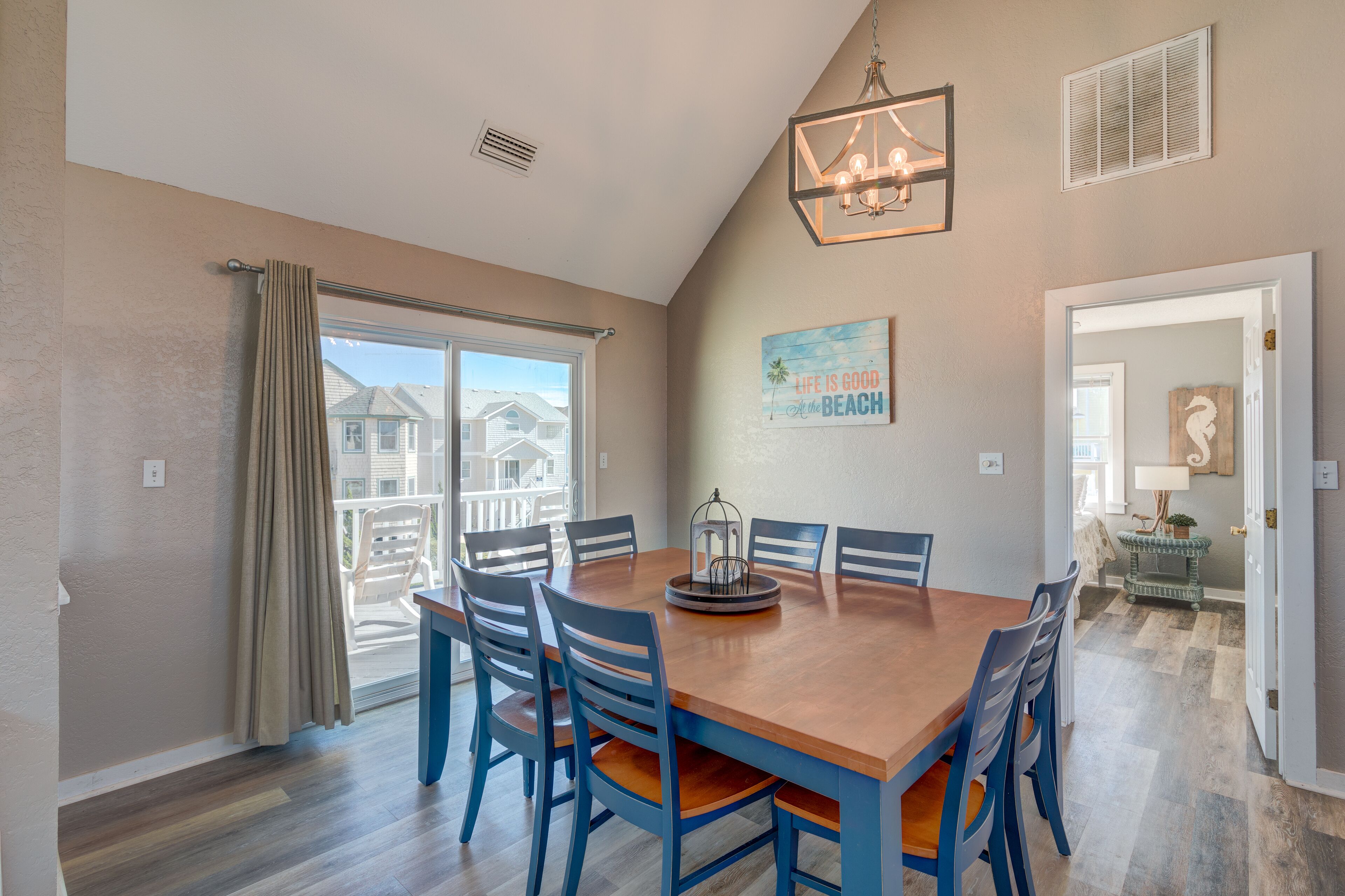 A dining area with a wooden table and blue chairs, a chandelier, and a painting on the wall.