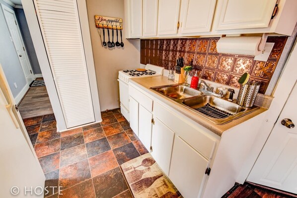 A compact kitchen with white cabinets, a gas stove, a sink, and a backsplash with a patterned tile design.