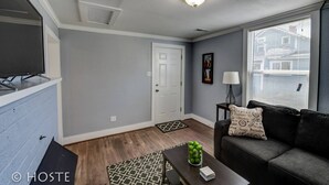 A living room with a flat-screen TV, a couch, a coffee table, and a window with blinds. - City Center Cottage Netflix, Mtns & Adventure! (Colorado Springs)