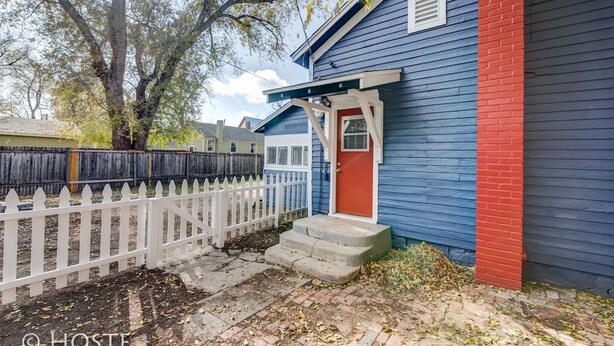 A house with a blue exterior and a red door, a white picket fence, and a brick pathway leading to the entrance. - City Center Cottage Netflix, Mtns & Adventure! (Colorado Springs)