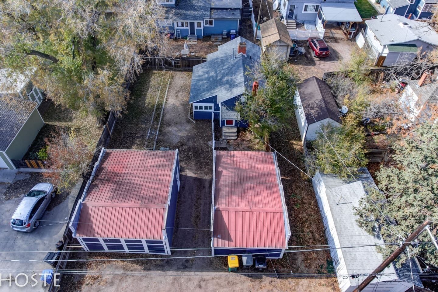 An aerial view of a residential area with two main buildings featuring red roofs, surrounded by trees and other houses.