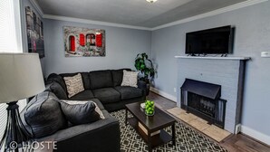 A living room with a fireplace, a sofa, a coffee table, and a TV mounted above the fireplace. - City Center Cottage Netflix, Mtns & Adventure! (Colorado Springs)