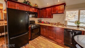 Une cuisine avec des meubles de rangement en bois, un réfrigérateur noir, une cuisinière et un lave-vaisselle.