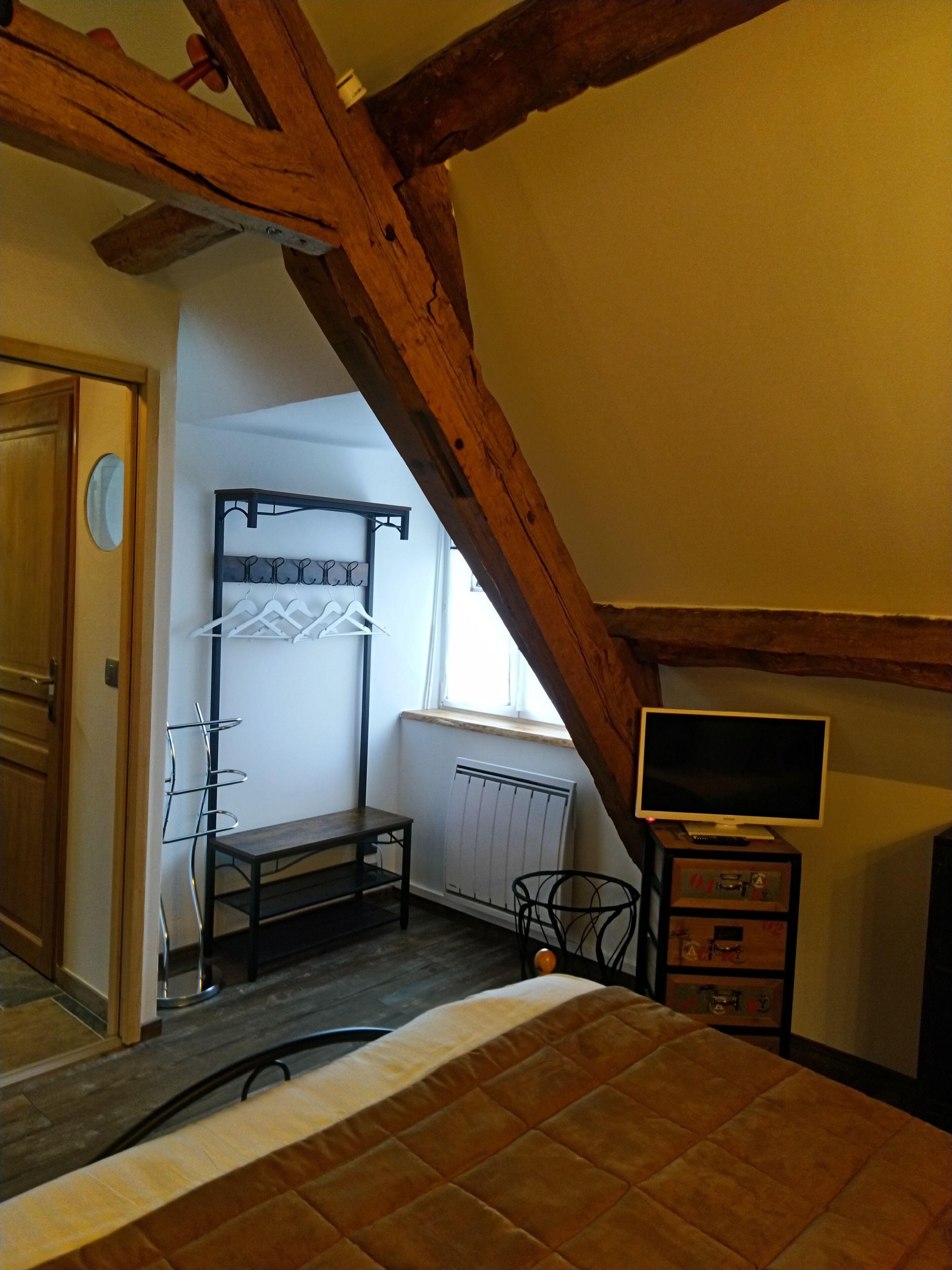 Een slaapkamer met een schuine kap, een bed, een tv-meubel en een radiator.