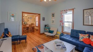 A living room with a blue sofa, a coffee table, a dining area with a wooden table and chairs, and a ceiling fan. - Downtown 1900 Classic 3 Bedroom Value (Colorado Springs)