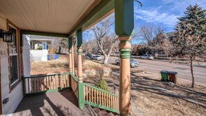 A covered porch with a wooden railing, a green door, and a clear view of a street with parked cars and trees. - Downtown 1900 Classic 3 Bedroom Value (Colorado Springs)