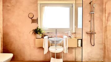 Un baño con lavamanos, espejo, ducha y planta en maceta.