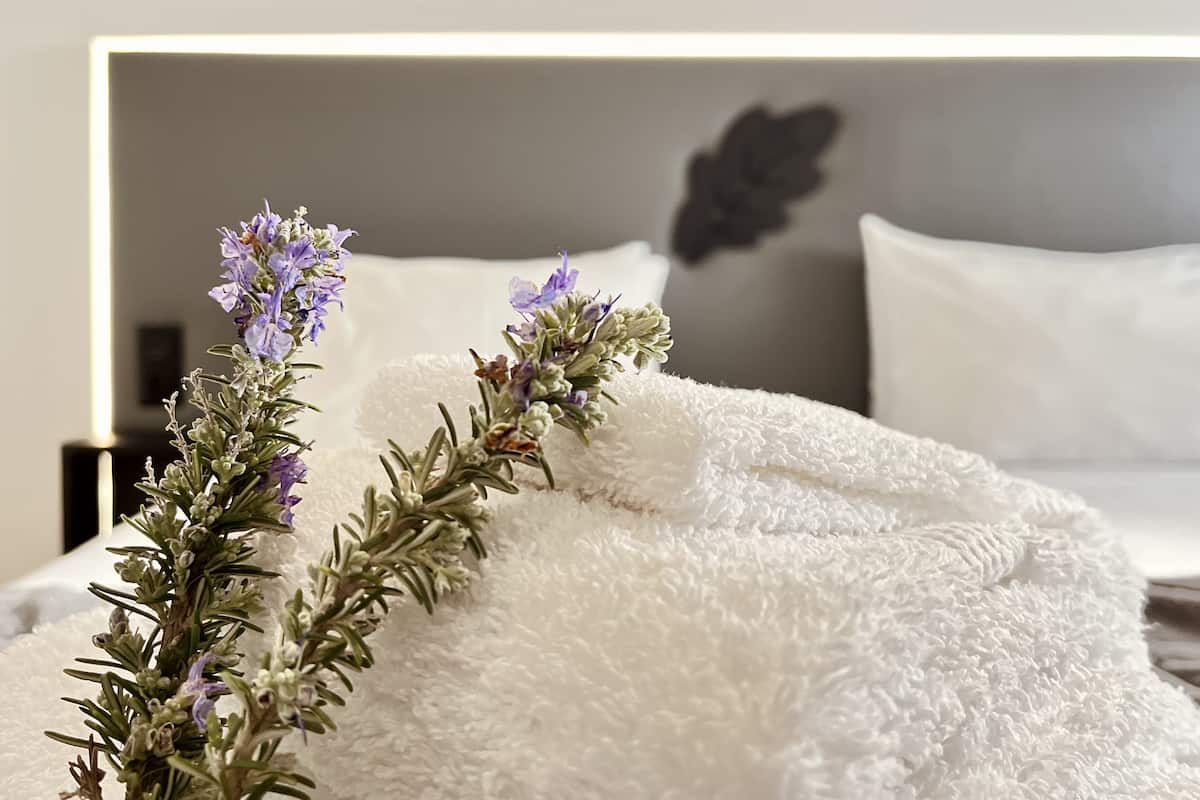 A neatly made bed with a white fluffy blanket and a sprig of lavender.